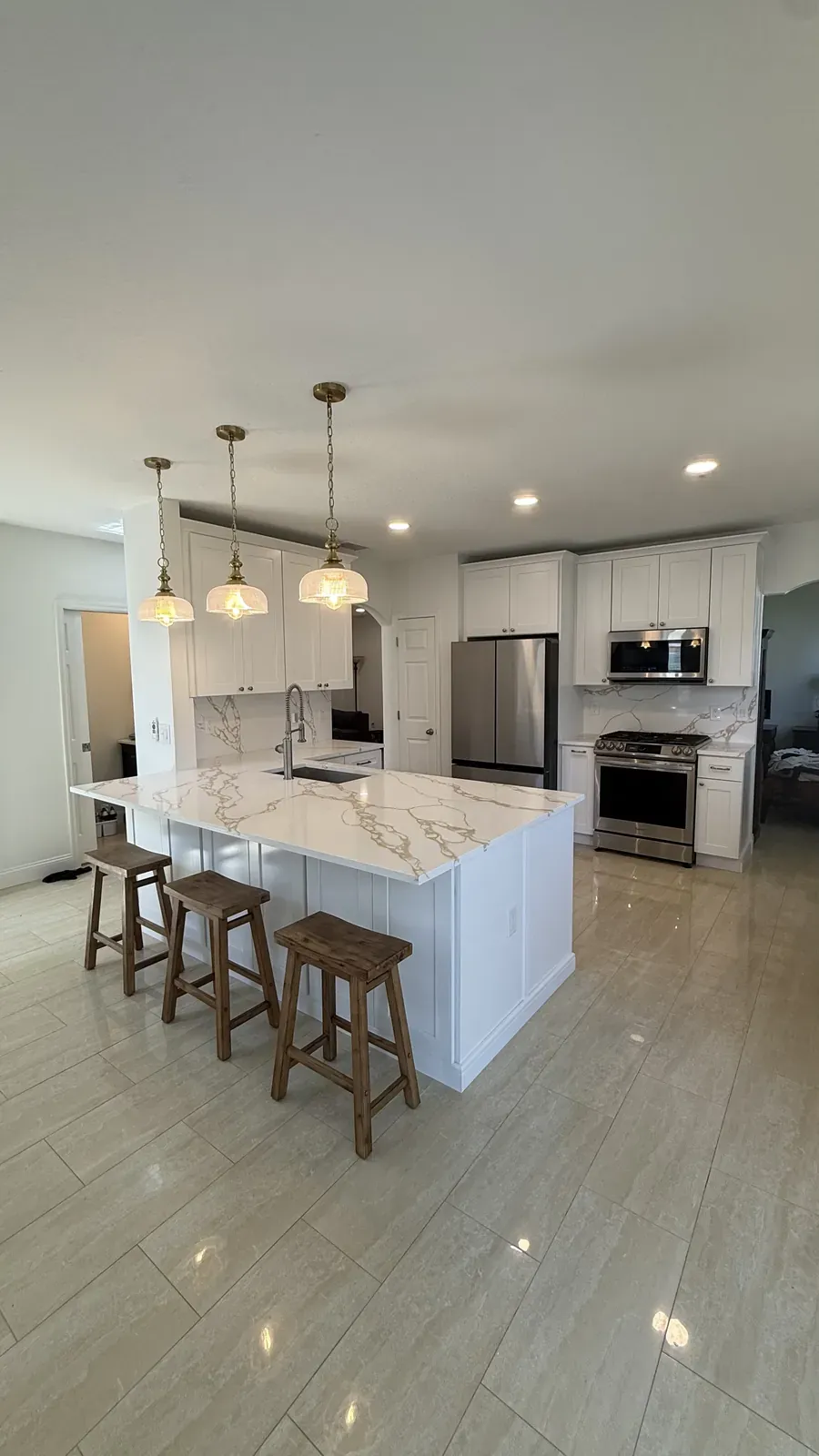 White shaker kitchen with a marble-look island, stainless appliances, and three brass pendant lights