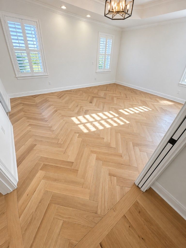 Bright room with a light oak herringbone floor, plantation shutters, and a lantern chandelier Bright room with a light oak herringbone floor, plantation shutters, and a lantern chandelier
