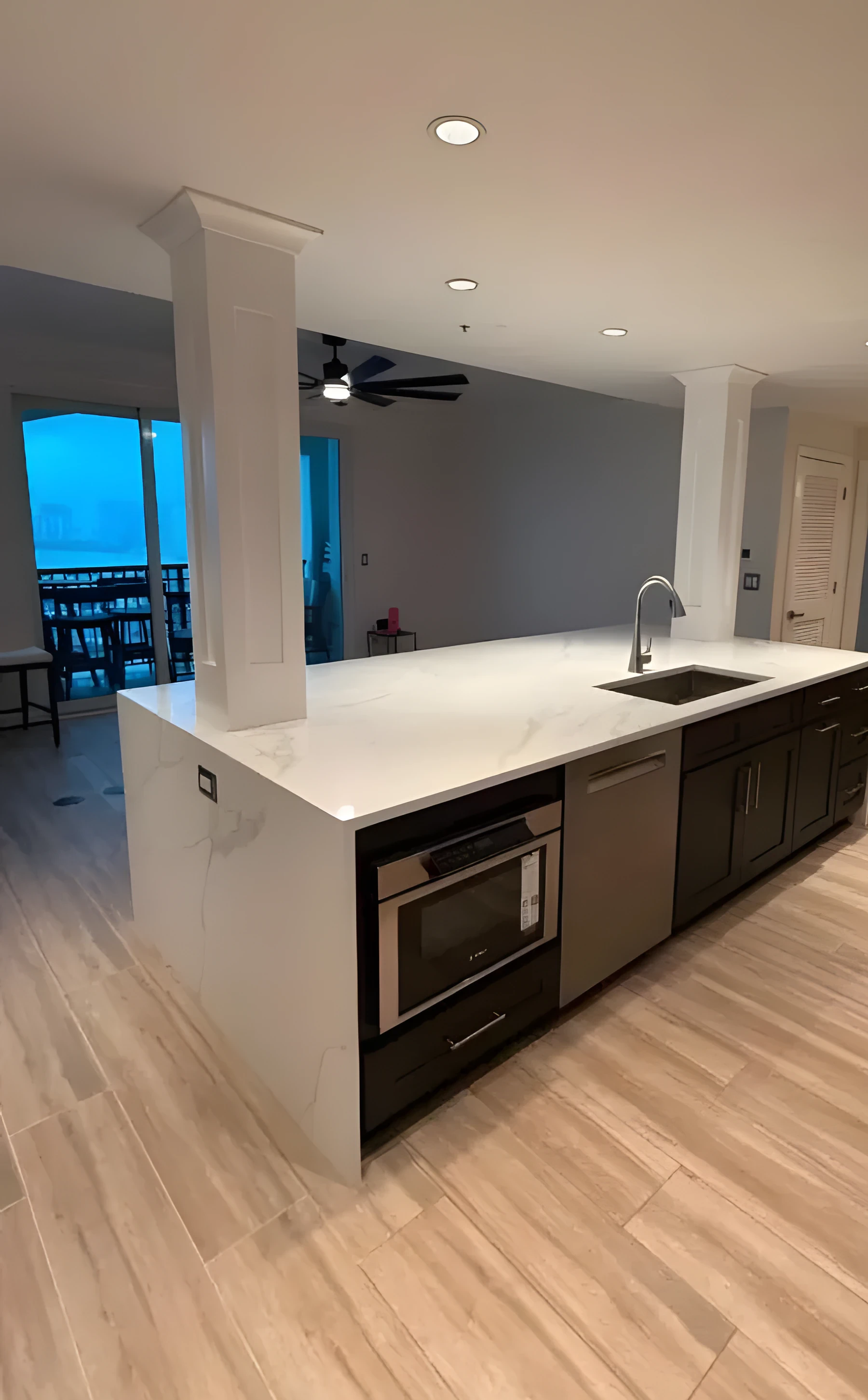 Kitchen island with a waterfall quartz counter, dark cabinets, and light wood-look flooring