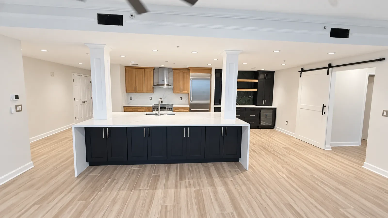 Open kitchen and living space with a navy island, a white waterfall counter, square columns, and a barn door