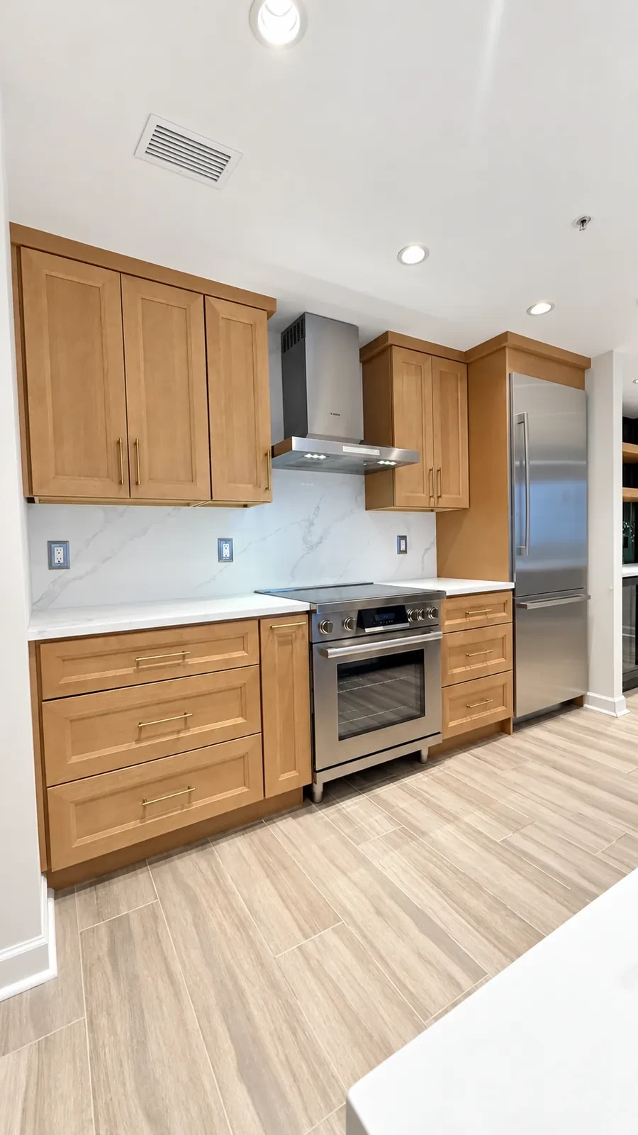 Oak shaker kitchen cabinets with brushed pulls, a stainless range, and a chimney hood
