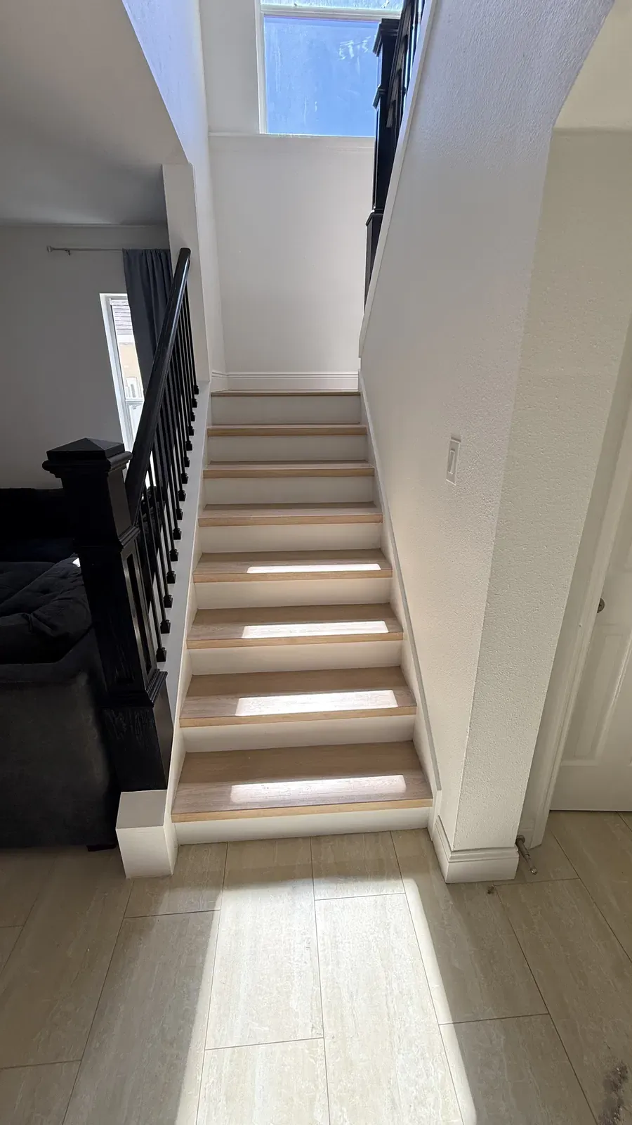 Light oak stair treads with white risers and a black handrail, lit by an upper window Light oak stair treads with white risers and a black handrail, lit by an upper window