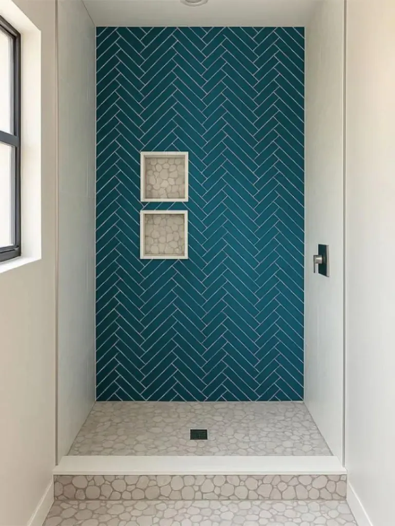 Shower wall in teal herringbone tile with pebble-lined niches Shower wall in teal herringbone tile with pebble-lined niches