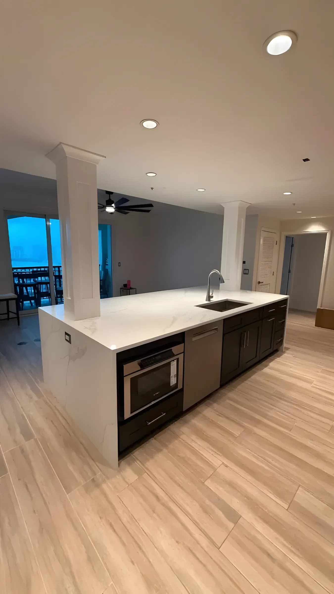 Kitchen island with a waterfall quartz counter, dark cabinets, and light wood-look flooring