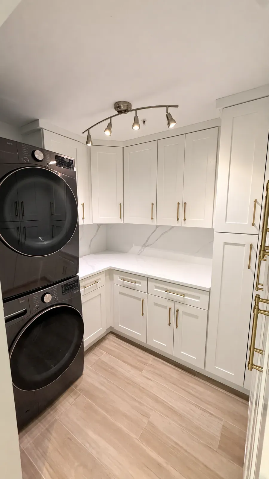 Laundry room with white shaker cabinets, brass pulls, a white stone counter, and a stacked washer and dryer Laundry room with white shaker cabinets, brass pulls, a white stone counter, and a stacked washer and dryer